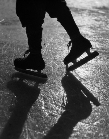1930s silhouette figure shown from knees down wearing ice skates skating in ice sun glare